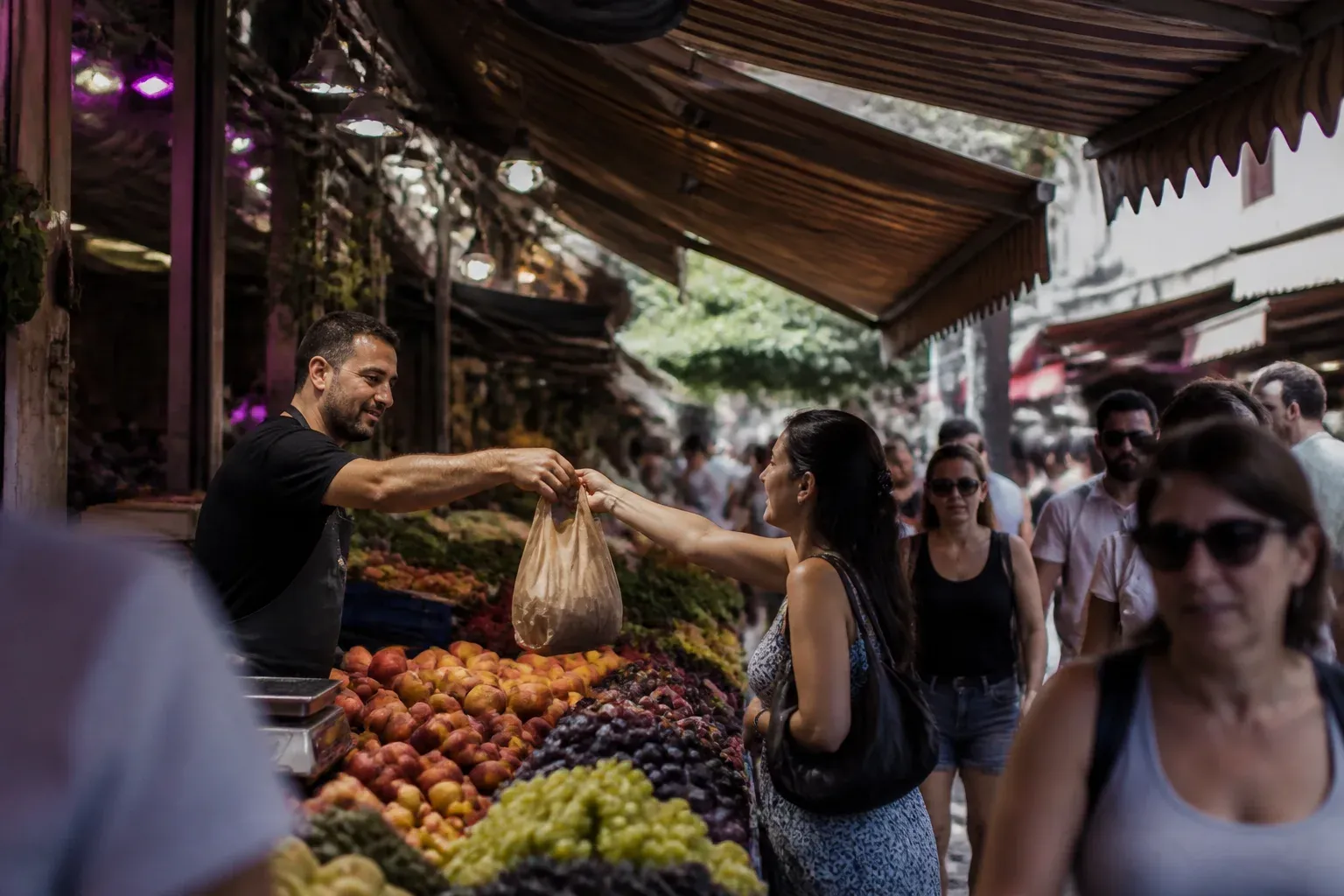 רוכל בשוק מקורה מגיש שקית ללקוחה בזמן שעוברים ליד הדוכן אנשים