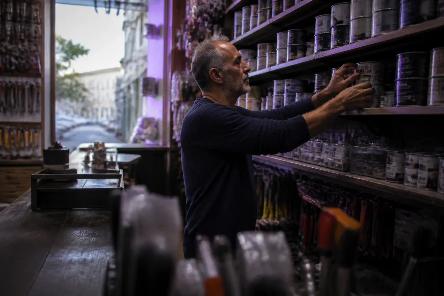 בעל חנות כלי עבודה עומד מאחורי הדלפק ומסדר מדפים מסודרים