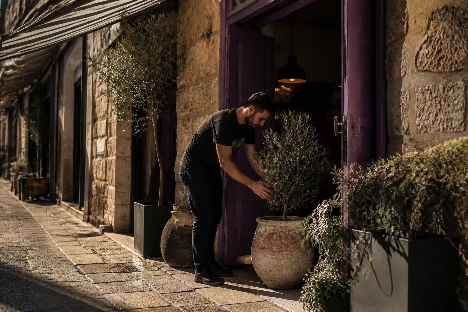 חנות צרה ברחוב עם סוכך ודלת פתוחה, גבר תולה סוכך בכניסה